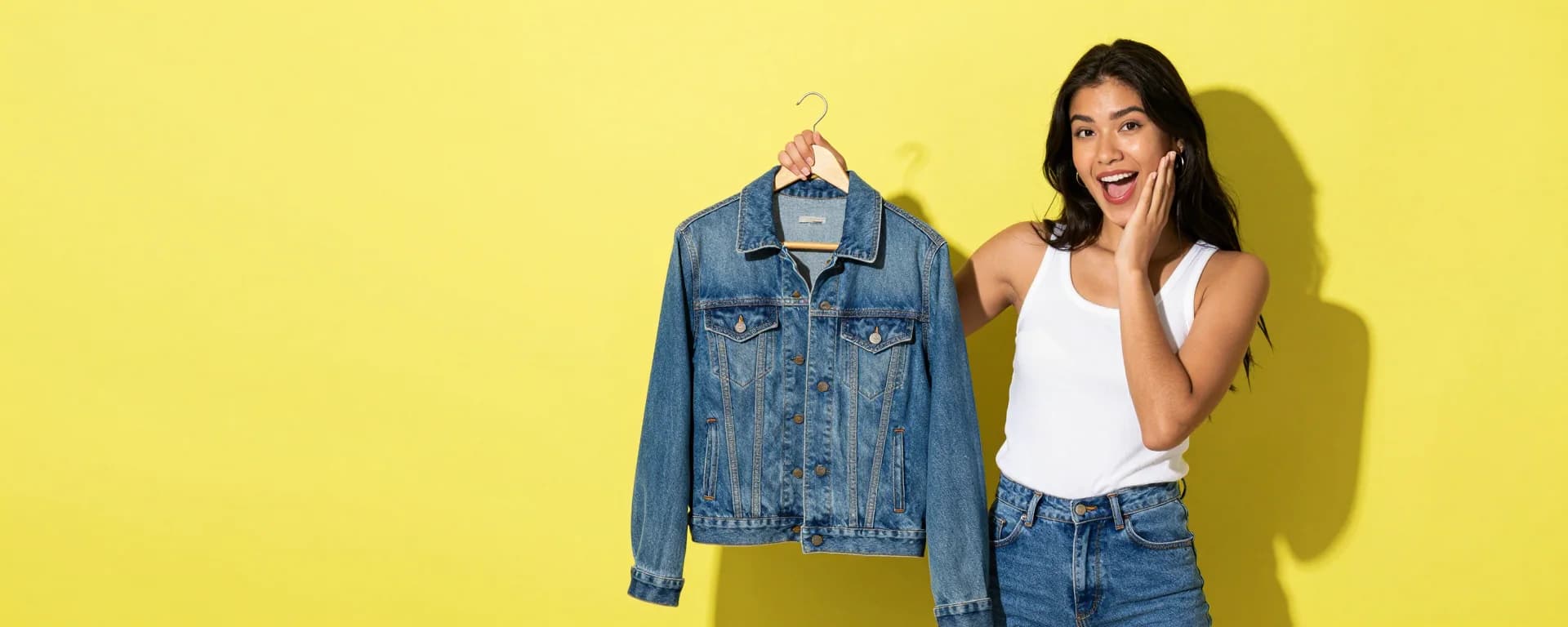Chica sonriendo sorprendida mientras sostiene una chamarra de denim vintage en un gancho